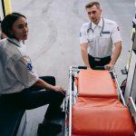 Dois socorristas preparam uma maca dentro de uma ambulância para um atendimento de emergência.