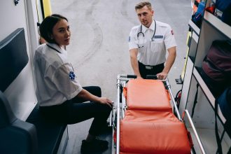 Dois socorristas preparam uma maca dentro de uma ambulância para um atendimento de emergência.
