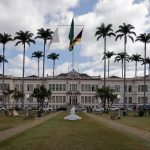 Fachada de um prédio municipal cercado por palmeiras sob céu nublado.