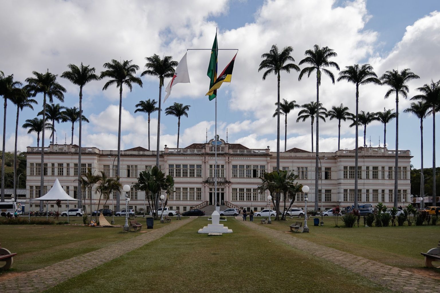 Fachada de um prédio municipal cercado por palmeiras sob céu nublado.