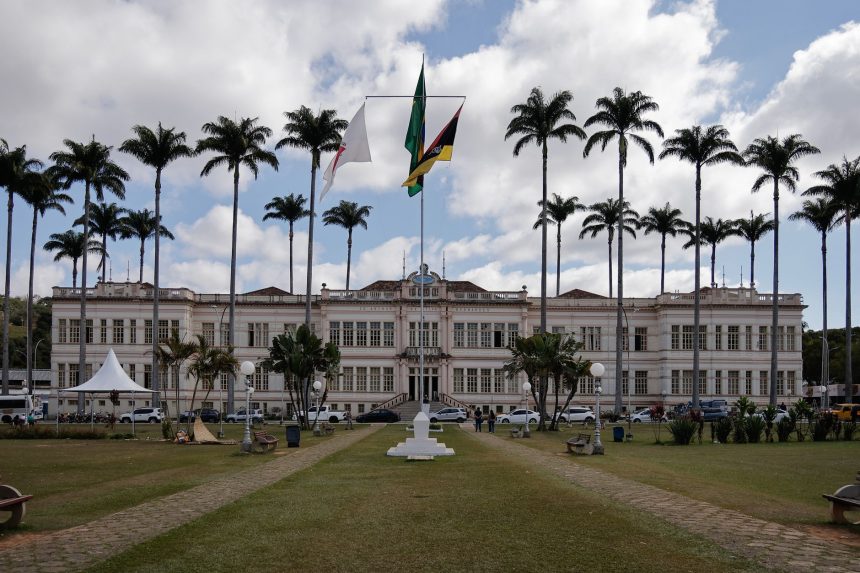 Fachada de um prédio municipal cercado por palmeiras sob céu nublado.